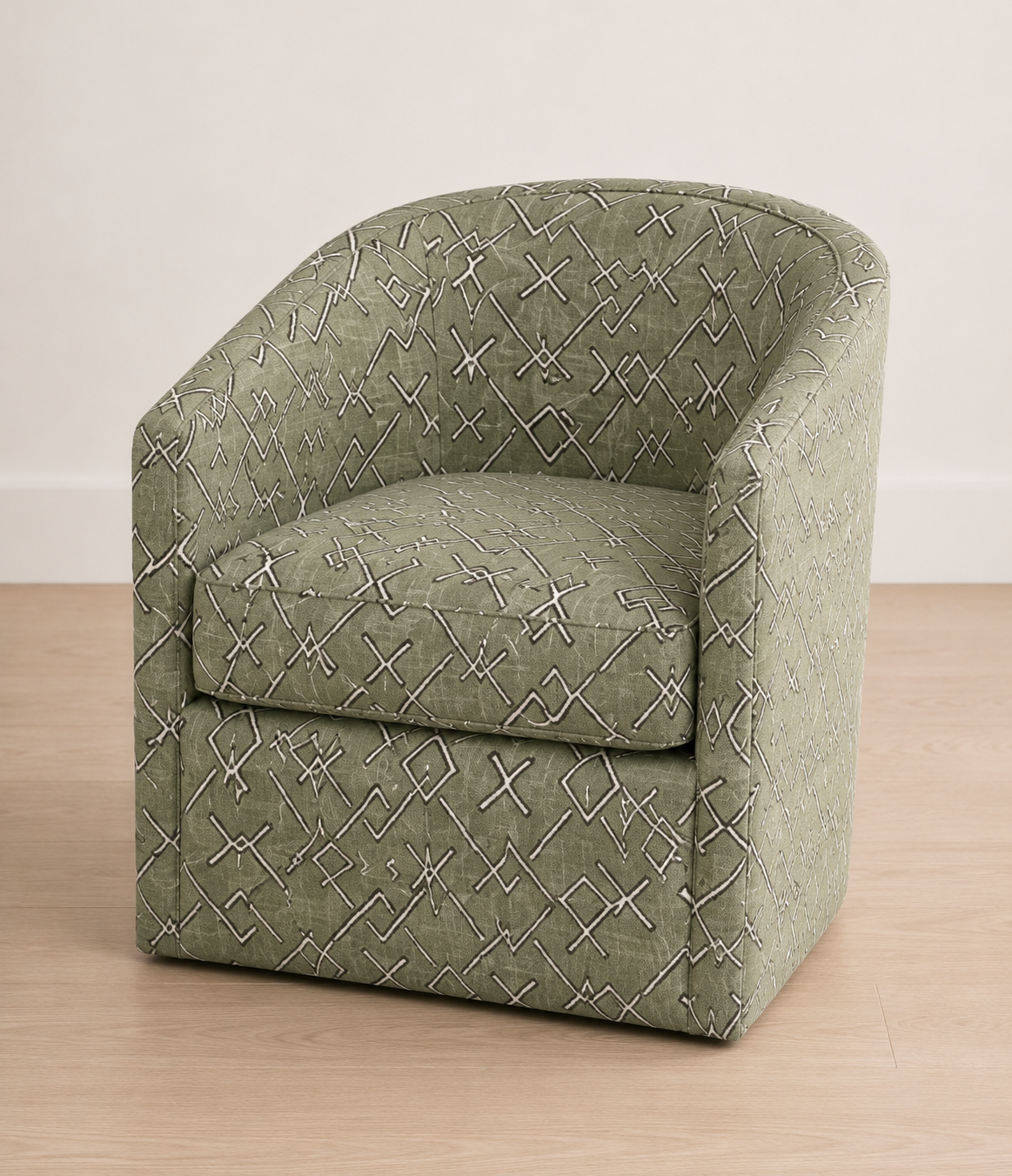 An upholstered barrel-style accent chair in sage green fabric with a white geometric diamond pattern, shown on a light wood floor against a neutral off-white wall.