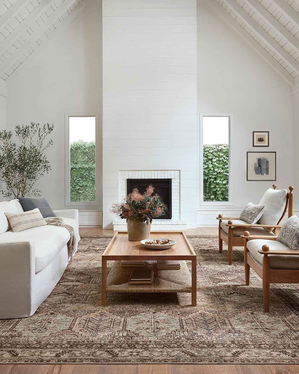 Bluffton-inspired living room with neutral seating, wood ceiling, white fireplace, and layered designer rug.