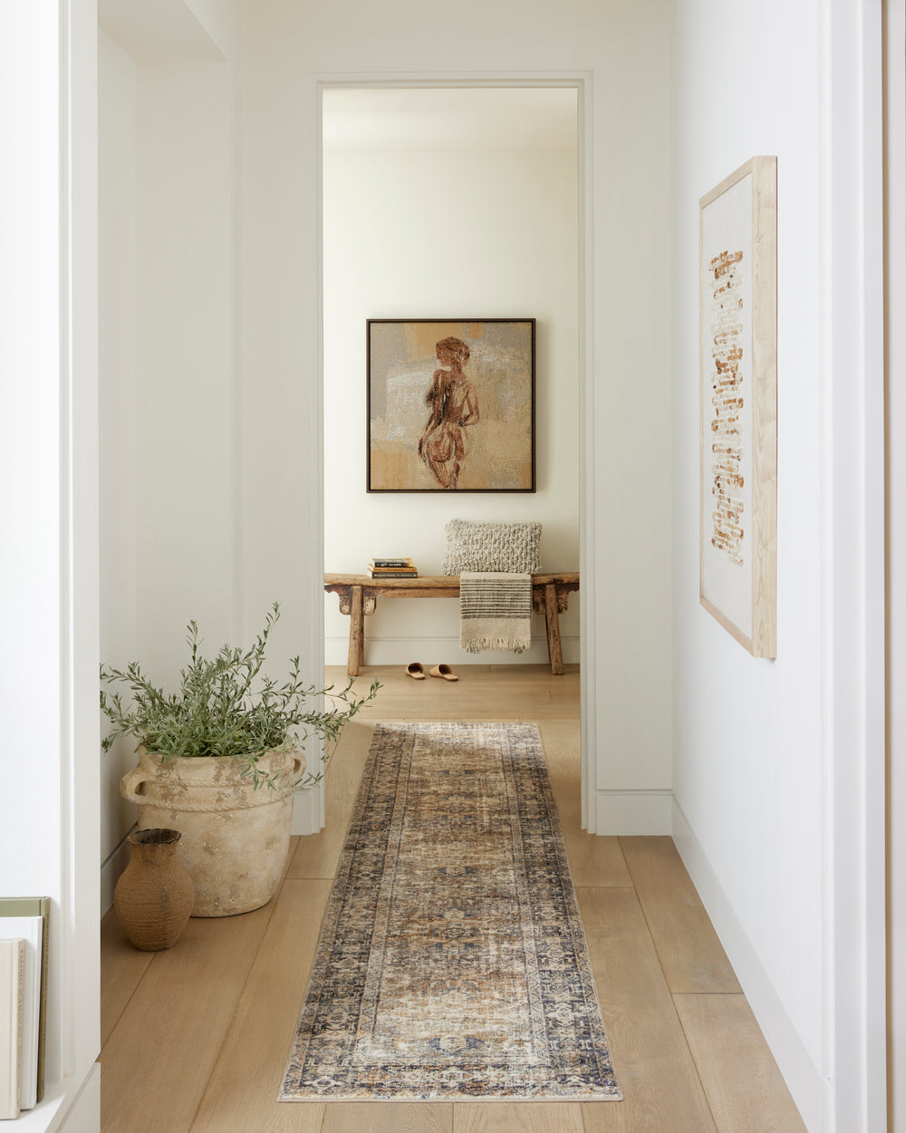 Light hallway with vintage-inspired runner rug, framed wall art, greenery, and natural wood details.