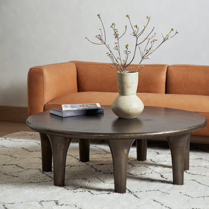 Round wooden coffee table with a vase and branches in front of an orange sofa.