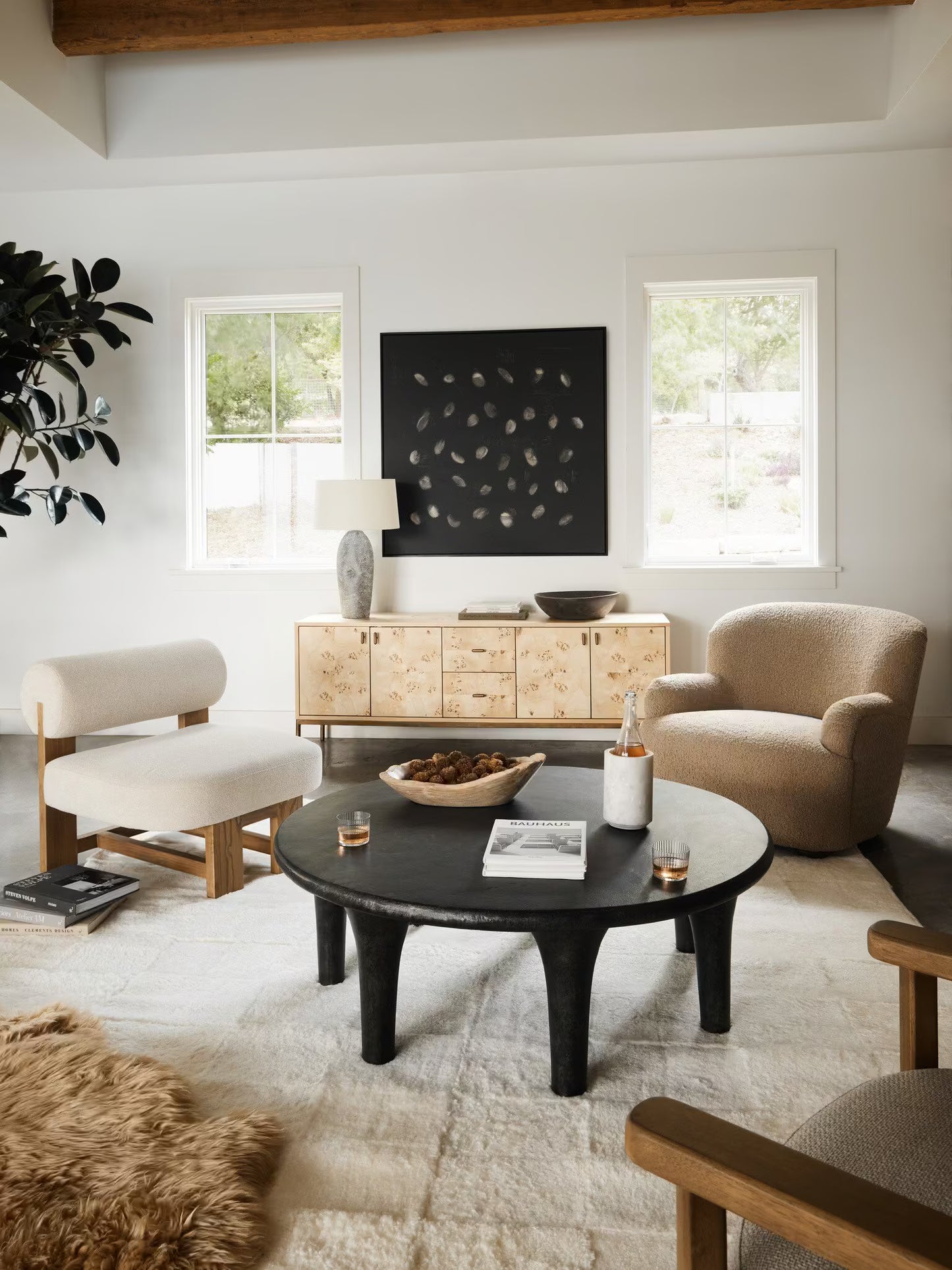 Modern living room with a black coffee table, beige armchairs, and a wooden sideboard.