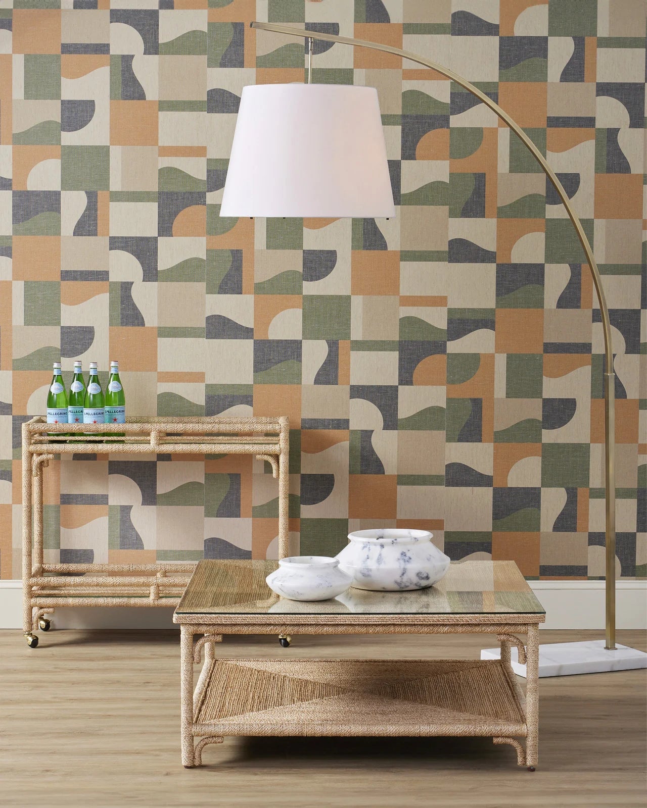 A large Cloister floor lamp with a white linen shade and brass base, featuring an acrylic diffuser, placed in a room with camouflage wallpaper.